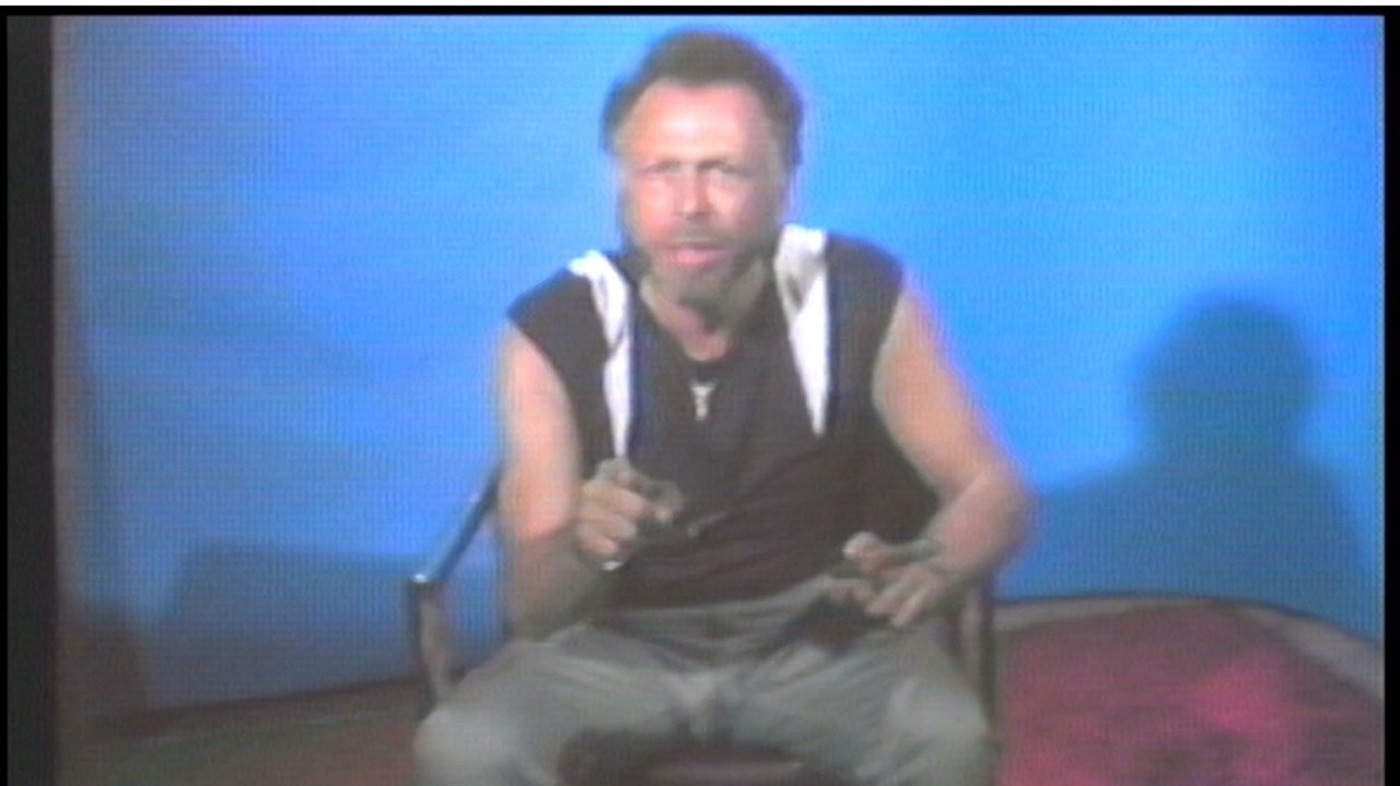 Man sitting on a chair, pointing at the camera